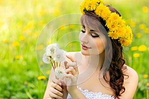 Beautiful girl with dandelion flowers in green field