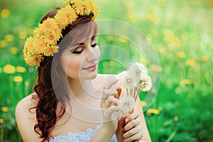 Beautiful girl with dandelion flowers in green field