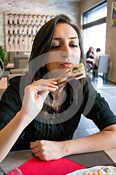 Beautiful girl with dark hair, dressed in black is holding chopsticks with sushi