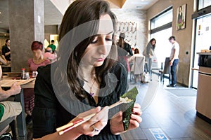 Beautiful girl with dark hair, dressed in black is holding chopsticks and temaki sushi
