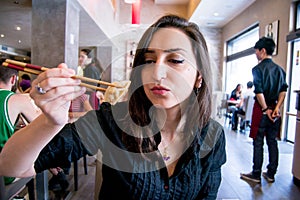 Beautiful girl with dark hair, dressed in black is holding meat ravioli with chopsticks