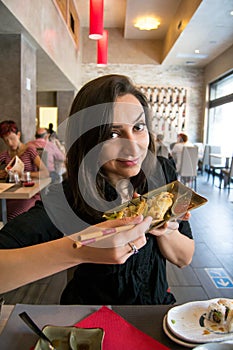 Beautiful girl with dark hair, dressed in black is holding a plate full of meat rolls and chilly sauce