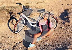 Beautiful girl with dark hair sitting beside a bicycle on beach