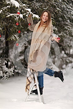 Beautiful girl decorates the Christmas tree with red balls in the forest. winter wood. Winter. Merry Christmas