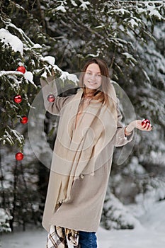 Beautiful girl decorates the Christmas tree with red balls in the forest. winter wood. Winter. Merry Christmas