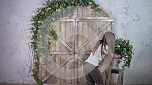 Beautiful girl decorator carries a vase of flowers and puts on a vintage small staircase against a beautiful photozone