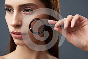 Beautiful girl demonstrating perfect skin through magnifying glass