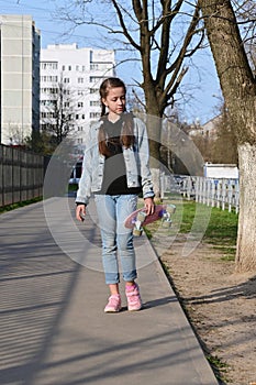 beautiful girl in denim clothes and pink sneakers. In the hand of a penny board, a longboard. International Skateboarding Day.