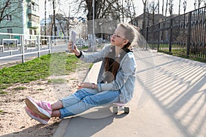 beautiful girl in denim and pink sneakers with a phone in her hand sits on a penny board, a longboard.