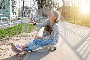beautiful girl in denim and pink sneakers with a phone in her hand sits on a penny board, a longboard. International Skateboarding