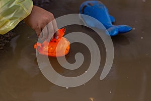 Beautiful girl in denim suit and yellow rubber boots plays with plastic duck and whale in a puddle