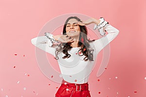 Beautiful girl with dimpled cheeks is smiling. Woman in stylish outfit smacks on pink background. photo