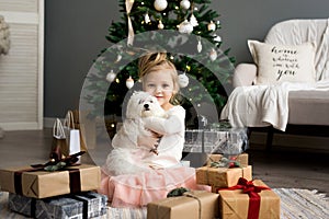 Beautiful girl with dog sitting near the Christmas tree. Merry Christmas and Happy Holidays.