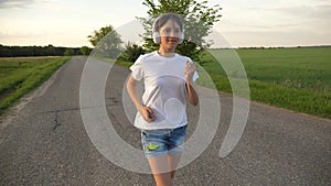 Beautiful girl doing sports exercises. girl in the music headphones runs along road. Slow motion