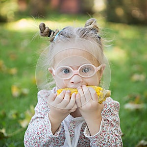 Beautiful girl with Down syndrome eating corn on the nature