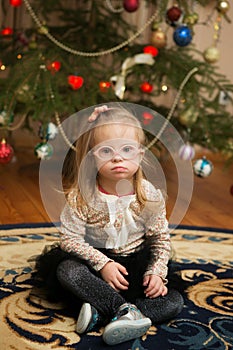 Beautiful girl with Down syndrome sits near a Christmas tree