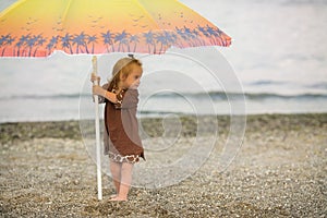 Beautiful girl with Down syndrome standing under an umbrella on the beach