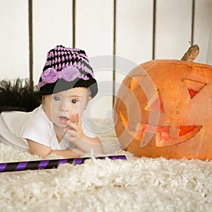 Beautiful girl with Down syndrome thoughtfully keeps finger in the mouth near the big pumpkin