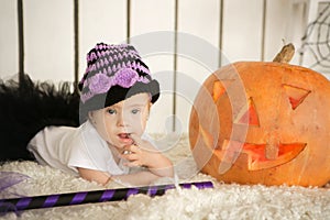 Beautiful girl with Down syndrome thoughtfully keeps finger in the mouth near the big pumpkin