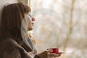 Beautiful girl dreaming with cup of coffee near window