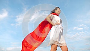 Beautiful girl dreams of becoming a superhero. sexy superhero girl standing on field in a red cloak, cloak fluttering in