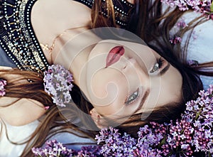 Beautiful girl in dress posing lying in lilac branches on a summer day, purple flowers in the Park. Spring portrait of a dreaming