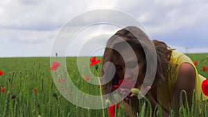 Beautiful girl in dress on wheat green field with red poppies is sniffing a flower. Slow motion outdoors