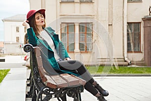 Beautiful girl dressed in a coat and hat resting, sitting on a bench with closed eyes.