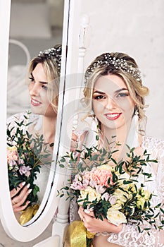 Beautiful girl dressed in peignoir and underwear sits on floor near mirror and holds bouquet in her hands.