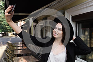 A beautiful girl dressed in a stylish white dress, a black jacket and a black hat is standing near the marble coffee table and a w