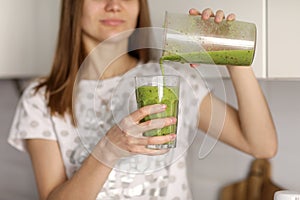 Beautiful girl drinks freshly prepared smoothie in kitchen. smoothies freshly made from assorted vegetable ingredients on kitchen