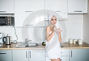 Beautiful girl drinks tea or coffee in the morning from a cup. Attractive young woman wrapped in towel in the kitchen after shower