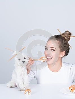 Beautiful girl eating japanese sushi rolls with chopsticks, funny dog, order in fastfood restaurant. Beauty woman with