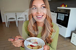 Beautiful girl eating muesli granola oatmeal with dried fruits and yogurt looking to the side at home