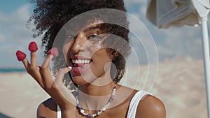 Beautiful girl eating raspberries of fingers closeup. Smiling woman rest beach