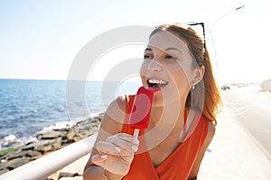 Beautiful girl eating a red popsicle on promenade beach on summer