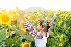 Beautiful girl in embrodery rise hands up on a sunflower plant