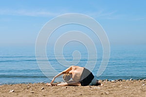 A beautiful girl is engaged in yoga on the beach against the background of the sea. Health and sports. A woman on the ocean shore