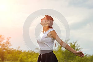 Beautiful girl enjoying the sun with her arms outstretched in the field against the sky