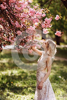 Beautiful girl enjoys the scent of flowering tree. Portrait of beautiful woman with blooming cherry tree - girl inhales