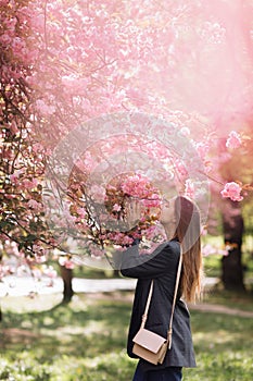 Beautiful girl enjoys the scent of flowering tree. Portrait of beautiful woman with blooming cherry tree - girl inhales