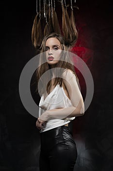 A beautiful girl with evening make-up and red lips wearing a blouse with a deep neckline and her hair suspended on chains, posing