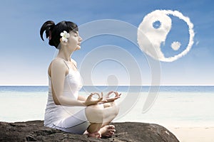 Beautiful girl exercise yoga at beach under ying yang cloud
