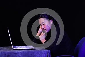 Beautiful girl faling asleep over her laptop on dark background