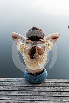 Beautiful girl with fashion clothes sits and resting on a wooden pier near the lake, summer holidays on nature