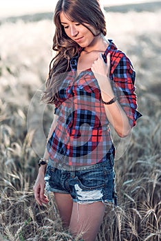 Beautiful girl field. Summer nature. Corrects long hair. In a shirt and shorts. A sunny day woman brunette, close-up