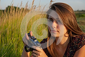 Beautiful girl with a film camera in her hands makes a photo in the meadow while traveling