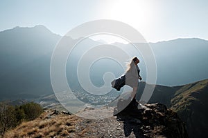 A beautiful girl in a flying dress is standing on a cliff overlooking the mountains