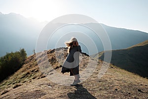 A beautiful girl in a flying dress is standing on a cliff overlooking the mountains