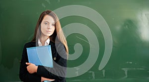 Beautiful girl with folder in hand on school green chalkboard background. Online education and e-learning concept. Back to school